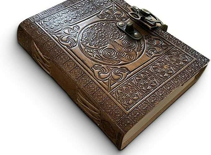Une photo représentant un cahier en cuir pouvant se fermer avec des dessins de style gothique.